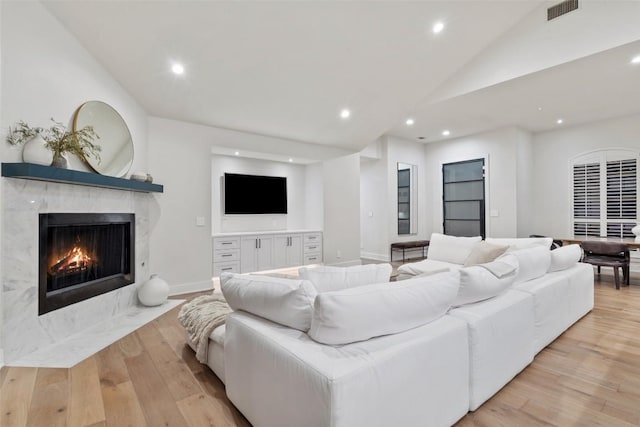 living room featuring recessed lighting, a high end fireplace, visible vents, vaulted ceiling, and light wood finished floors