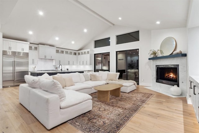 living room with recessed lighting, a fireplace with flush hearth, high vaulted ceiling, light wood-type flooring, and beamed ceiling