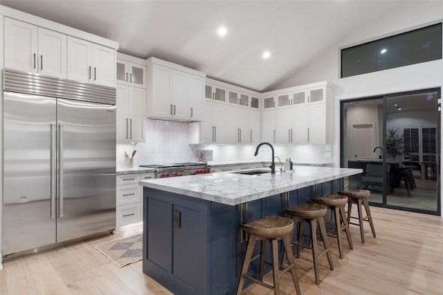 kitchen with light stone countertops, a sink, light wood-style floors, appliances with stainless steel finishes, and decorative backsplash