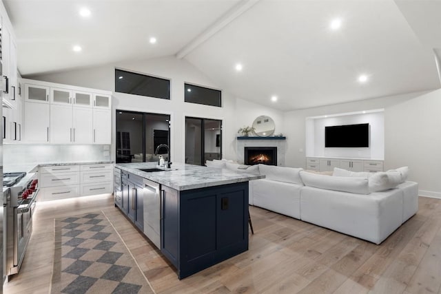 kitchen with light wood finished floors, a sink, stainless steel appliances, white cabinetry, and beam ceiling