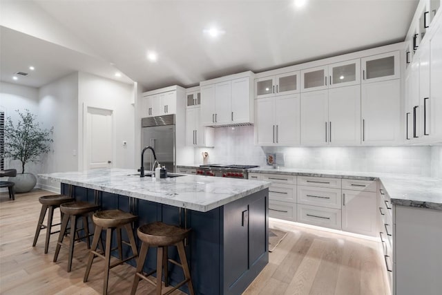 kitchen with light wood finished floors, stainless steel built in refrigerator, a sink, and a center island with sink