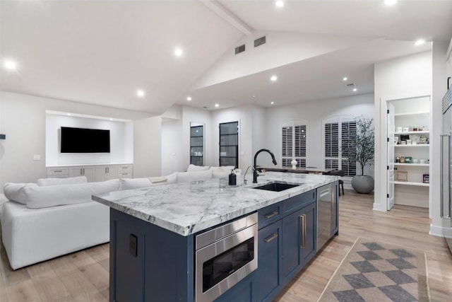 kitchen featuring stainless steel appliances, a sink, light wood-style floors, open floor plan, and blue cabinetry