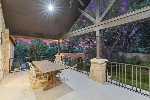 patio terrace at dusk with outdoor dining space, a fenced backyard, and a lawn