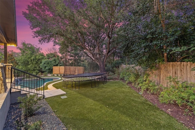 yard at dusk featuring a fenced backyard, a trampoline, a fenced in pool, and a patio