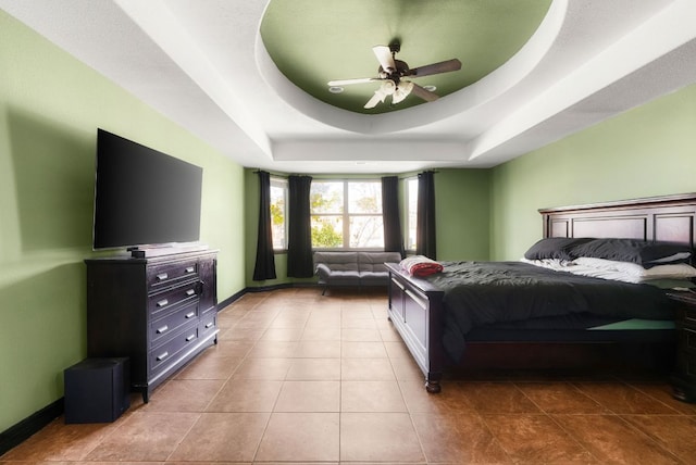 bedroom featuring a raised ceiling, light tile patterned flooring, ceiling fan, and baseboards