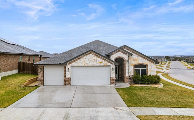 french country home with an attached garage, fence, concrete driveway, and a front yard