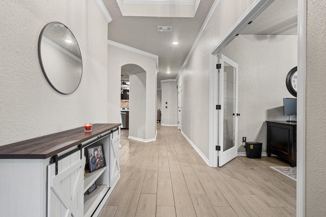 hallway featuring light wood-style floors, crown molding, and a textured wall