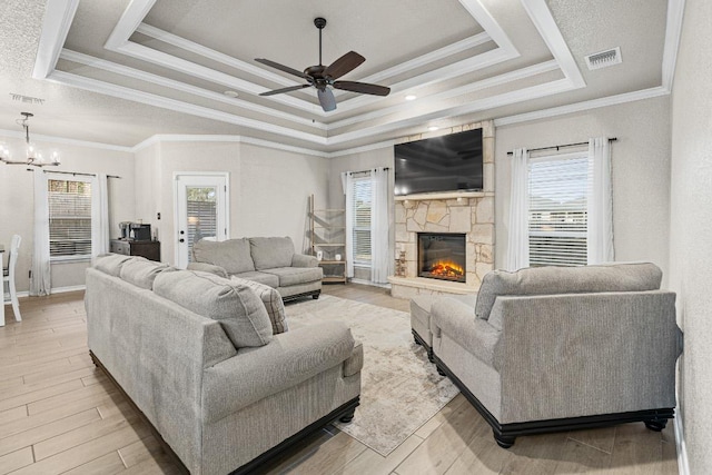 living area featuring a raised ceiling, visible vents, a fireplace, and light wood-style flooring