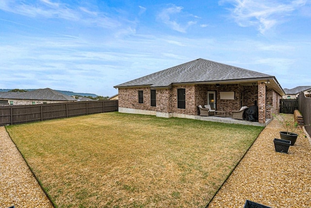 rear view of house with brick siding, a patio, a shingled roof, a lawn, and a fenced backyard