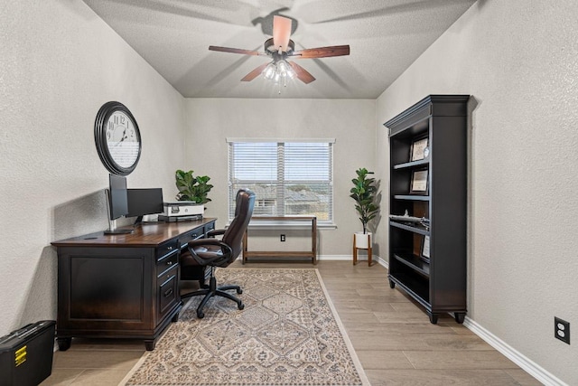 office space featuring a textured wall, baseboards, ceiling fan, and light wood finished floors