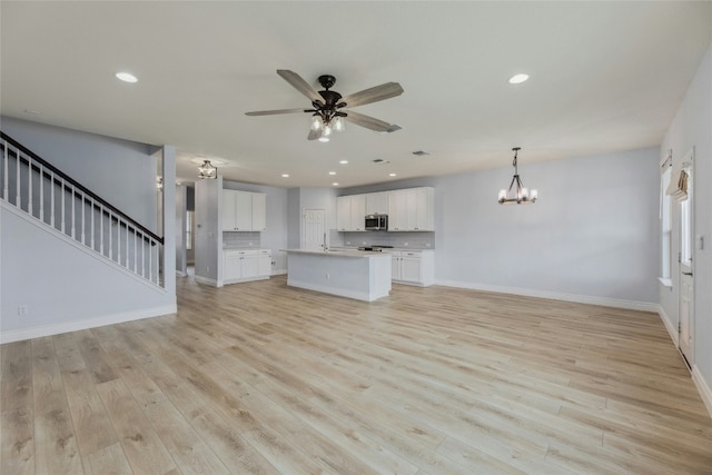 unfurnished living room with light wood-style flooring, stairs, baseboards, and ceiling fan with notable chandelier