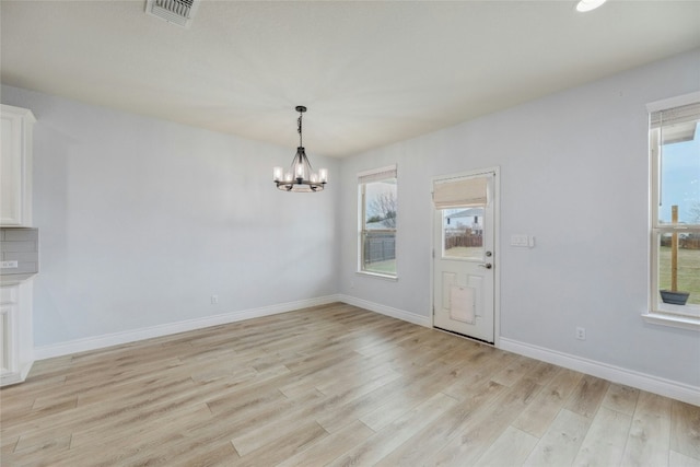 unfurnished dining area featuring light wood-type flooring, an inviting chandelier, baseboards, and visible vents