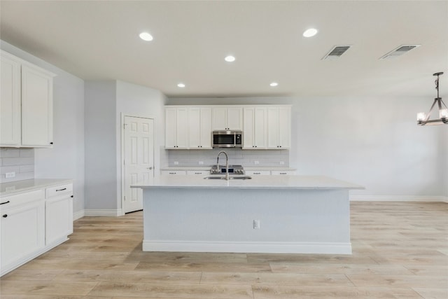 kitchen featuring visible vents, stainless steel microwave, light countertops, and a sink