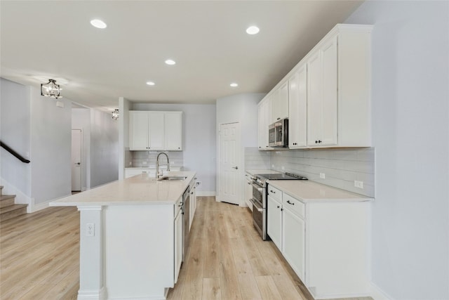 kitchen with white cabinets, light wood-style flooring, stainless steel appliances, and a sink