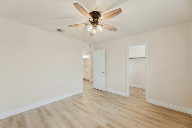 unfurnished bedroom featuring a walk in closet, baseboards, visible vents, and light wood finished floors