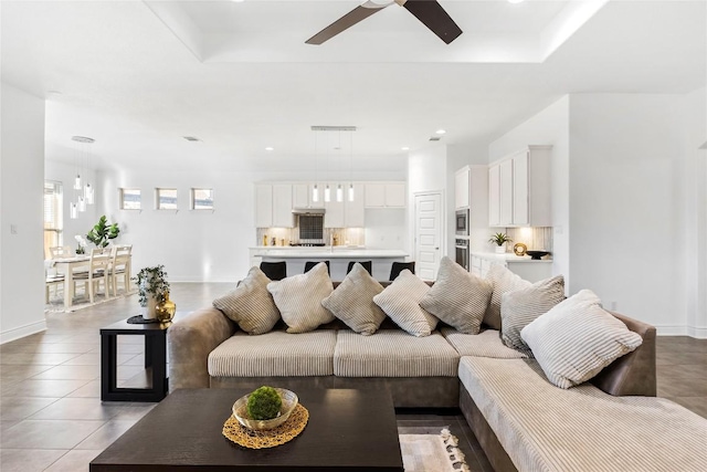 living area featuring light tile patterned floors, baseboards, a tray ceiling, and a ceiling fan