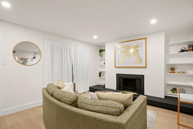 living room featuring light wood-style floors, baseboards, a fireplace, and built in features