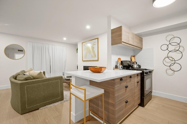 kitchen with a breakfast bar area, black gas range, light wood-style flooring, and baseboards