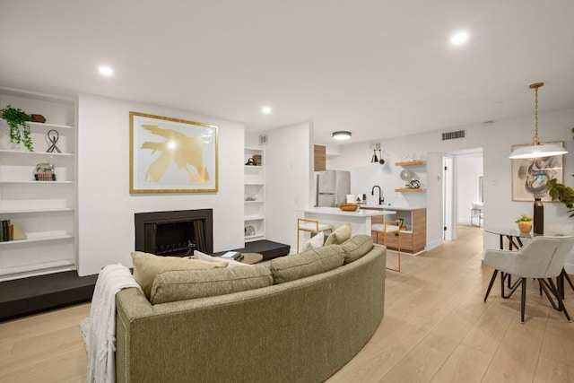 living room with light wood-style flooring, recessed lighting, a fireplace, visible vents, and built in features