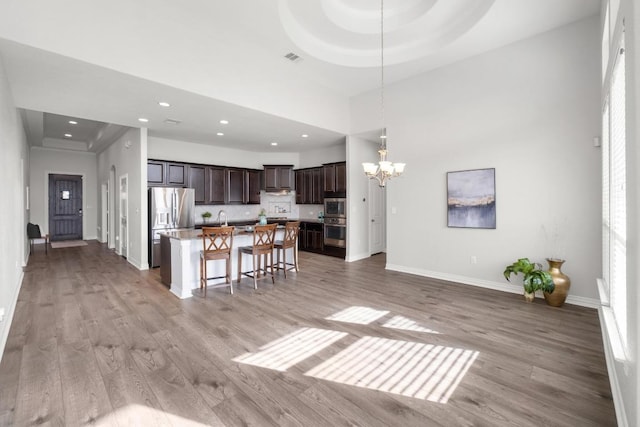 kitchen with dark brown cabinetry, a tray ceiling, stainless steel appliances, and a notable chandelier