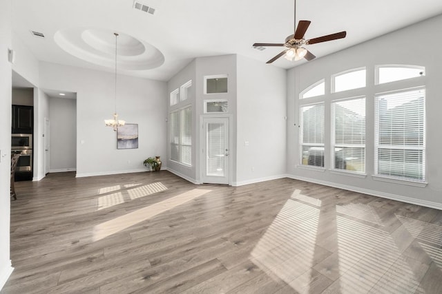 unfurnished living room featuring ceiling fan with notable chandelier, a raised ceiling, visible vents, and wood finished floors