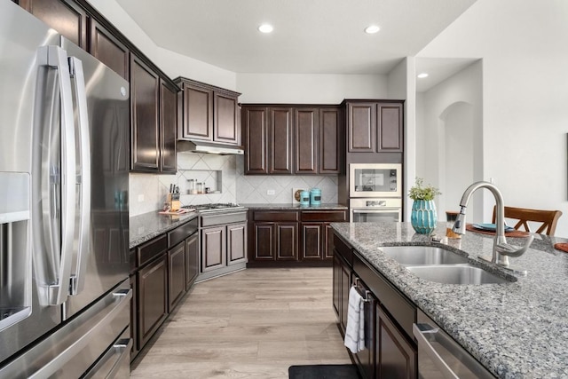 kitchen with stone counters, a sink, light wood-style floors, appliances with stainless steel finishes, and decorative backsplash