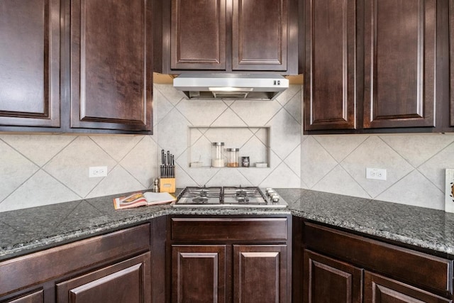 kitchen featuring stainless steel gas cooktop, decorative backsplash, dark stone countertops, dark brown cabinets, and exhaust hood