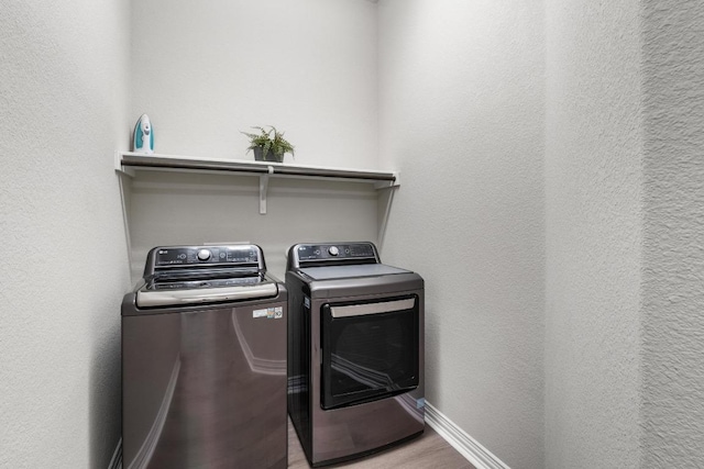 washroom featuring washer and dryer, laundry area, baseboards, and wood finished floors