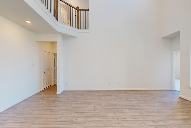 spare room featuring light wood-style flooring, recessed lighting, a towering ceiling, and baseboards