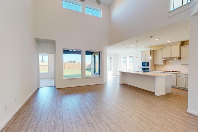 unfurnished living room with light wood finished floors, recessed lighting, a high ceiling, a ceiling fan, and baseboards