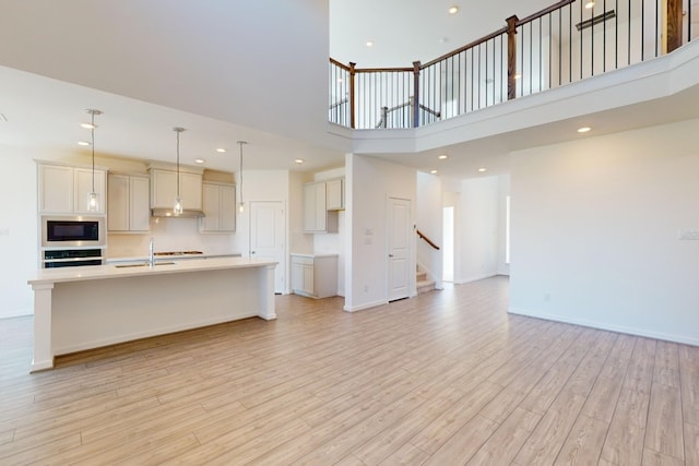 unfurnished living room featuring recessed lighting, stairway, a high ceiling, light wood-type flooring, and baseboards