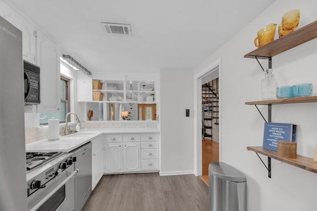 kitchen featuring black microwave, open shelves, a sink, and white cabinets