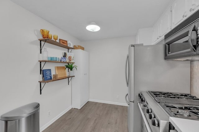 kitchen with black microwave, white cabinetry, light wood-style floors, stainless steel gas range, and open shelves