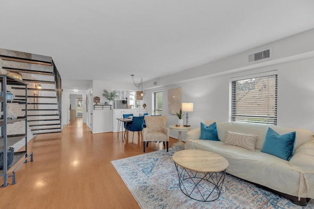 living room with light wood-style floors, visible vents, and stairs