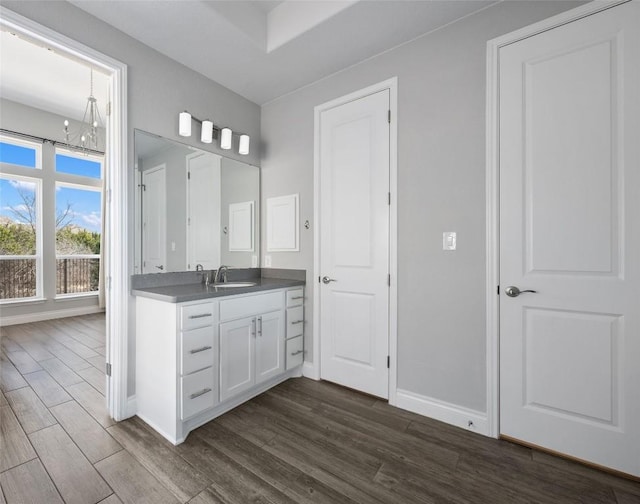 bathroom featuring a notable chandelier, wood finished floors, vanity, and baseboards