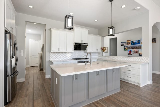 kitchen with tasteful backsplash, an island with sink, dark wood-style flooring, light countertops, and stainless steel refrigerator with ice dispenser