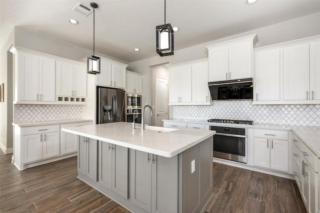 kitchen featuring visible vents, appliances with stainless steel finishes, dark wood-type flooring, a kitchen island with sink, and a sink