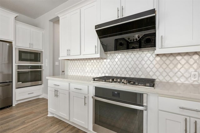 kitchen with light wood finished floors, white cabinets, decorative backsplash, appliances with stainless steel finishes, and ventilation hood