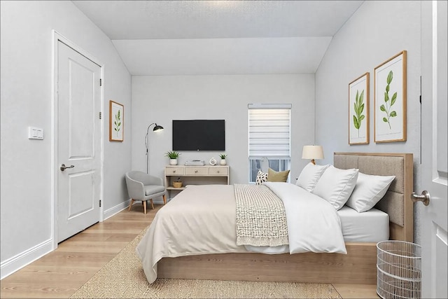 bedroom featuring light wood finished floors, baseboards, and vaulted ceiling