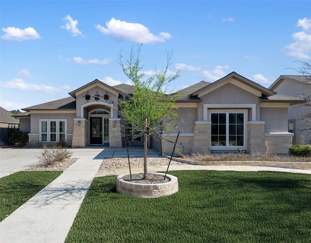 view of front of property featuring a shingled roof, stone siding, a front lawn, and stucco siding