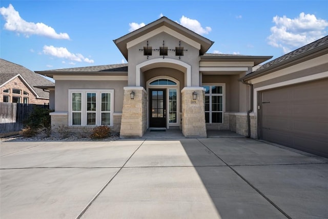 view of exterior entry with driveway, a garage, stone siding, fence, and stucco siding