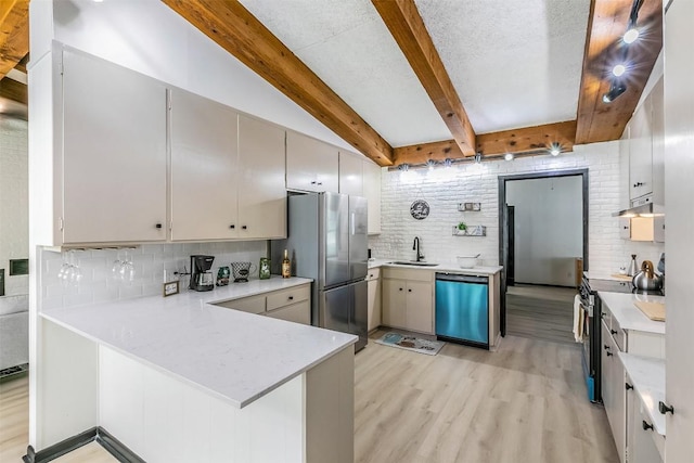 kitchen featuring tasteful backsplash, light countertops, appliances with stainless steel finishes, a sink, and a peninsula