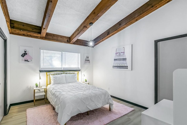 bedroom with vaulted ceiling with beams, light wood-style floors, and baseboards