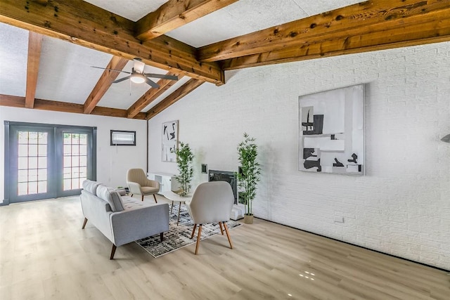 living room featuring ceiling fan, vaulted ceiling with beams, brick wall, and wood finished floors