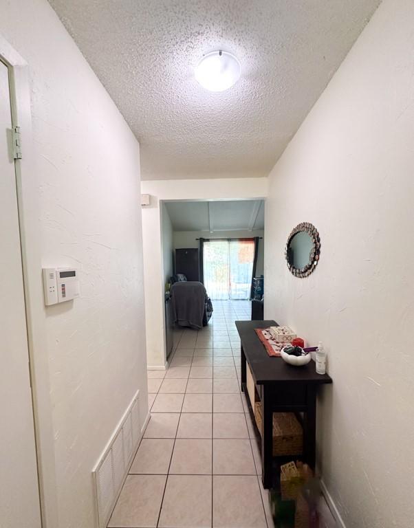 hall featuring a textured ceiling, light tile patterned flooring, visible vents, and baseboards