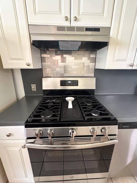 kitchen featuring dark countertops, backsplash, stainless steel range with gas stovetop, white cabinetry, and under cabinet range hood