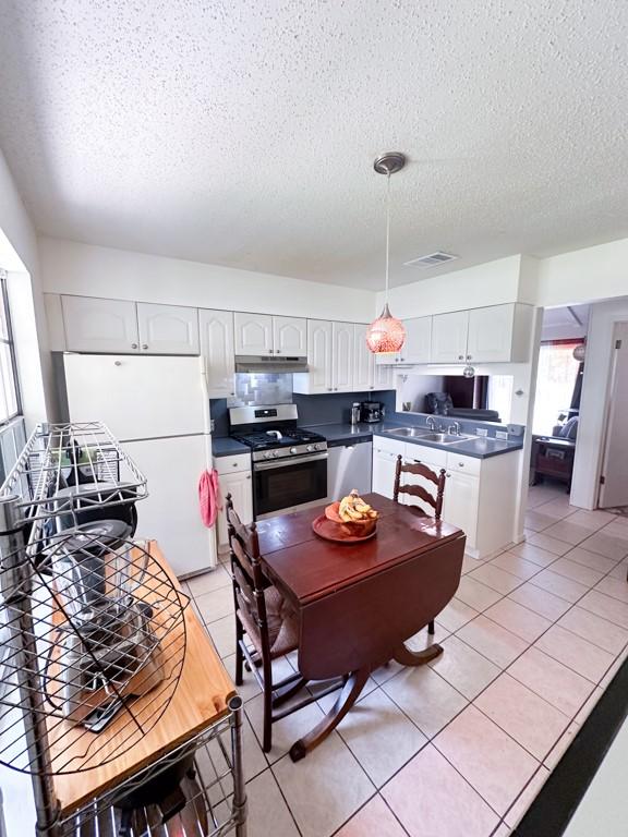 kitchen featuring light tile patterned floors, stainless steel appliances, dark countertops, visible vents, and under cabinet range hood