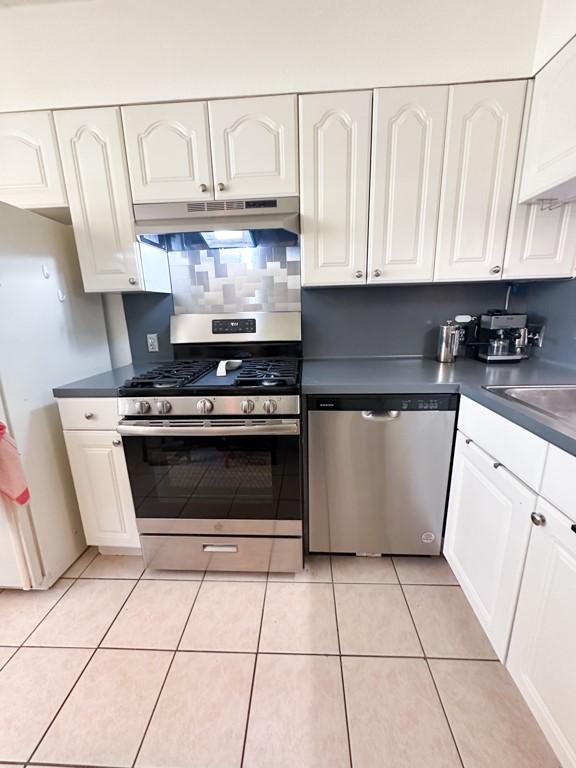 kitchen with appliances with stainless steel finishes, dark countertops, white cabinetry, and under cabinet range hood