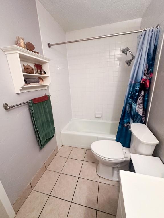 bathroom featuring a textured ceiling, shower / bath combination with curtain, toilet, and tile patterned floors