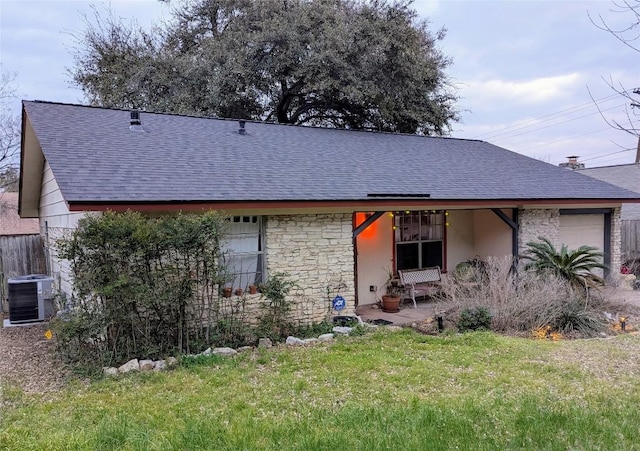 view of front of property with an attached garage, a shingled roof, a front yard, and cooling unit